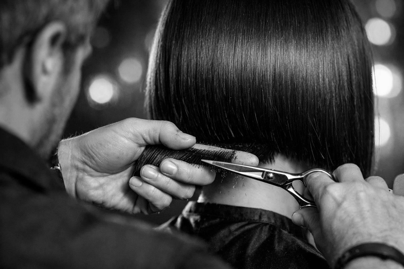 Black and white close-up of scissors cutting a clean line on a bob haircut